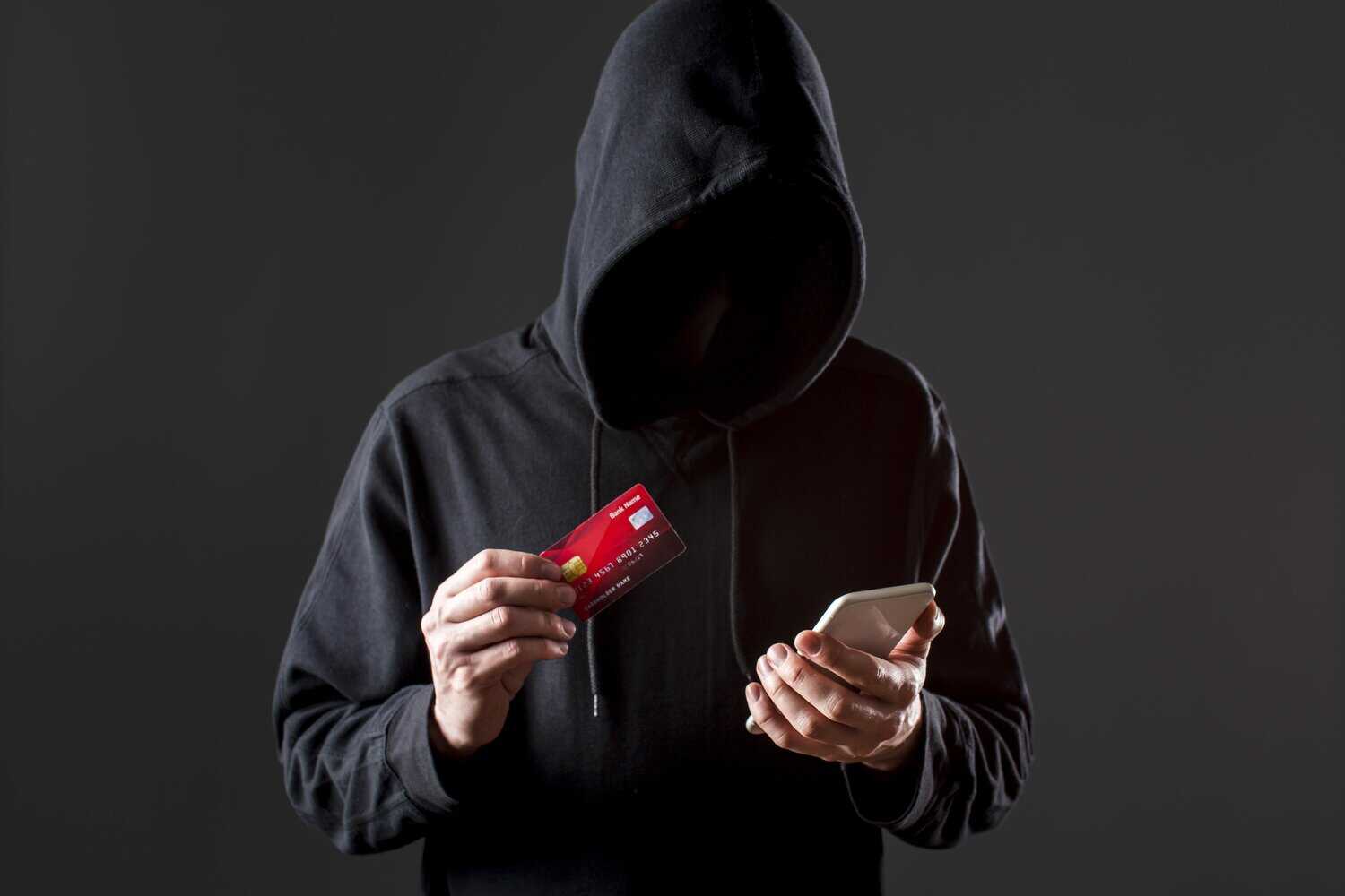 Anonymous fraudster with credit card and phone illustrating payment fraud threats